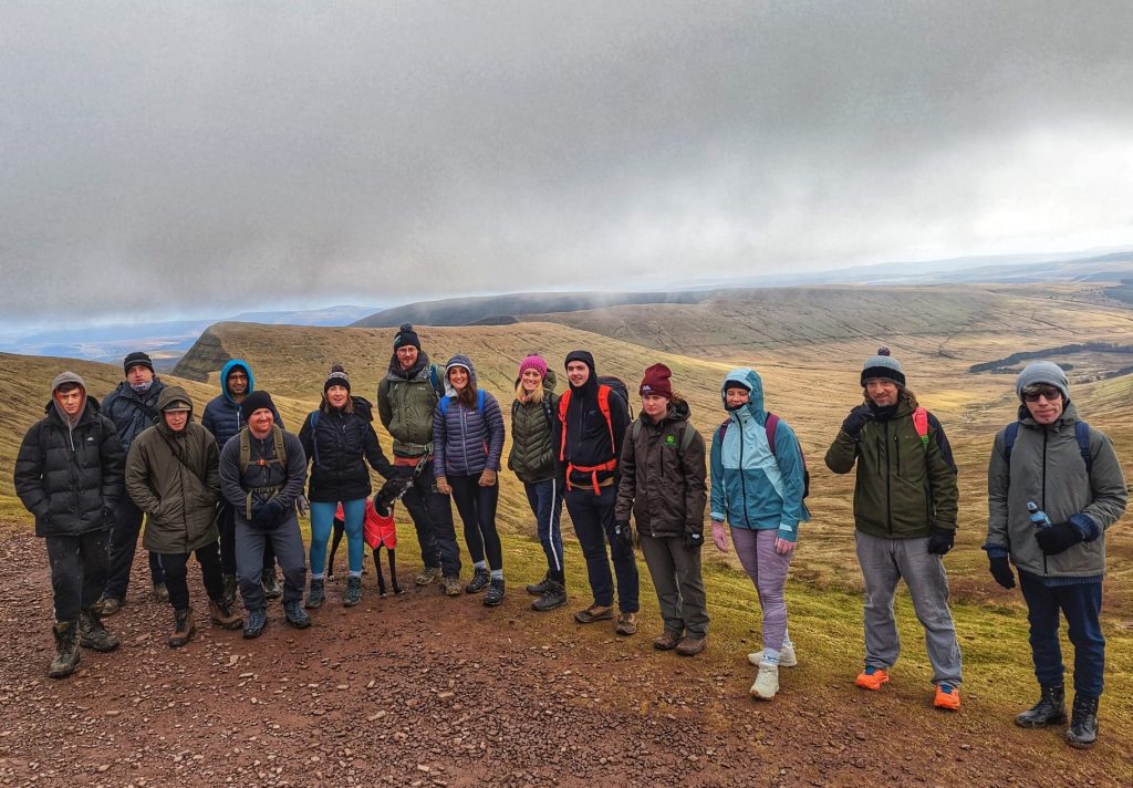 people standing in a row wearing hiking gear with the Pen y fan hills and grey clouds behind them