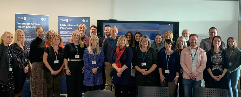 A group photo of two rows of people smiling at the camera in front of banners that read Early Intervention in Psychosis