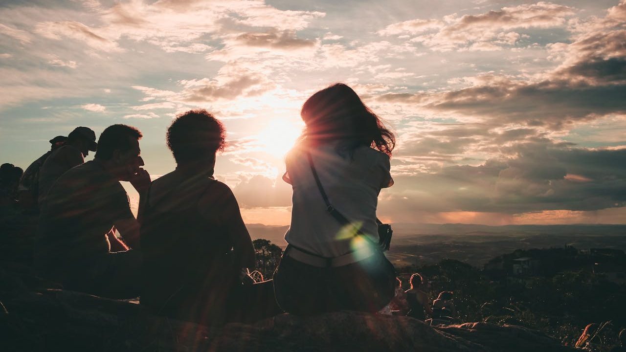 A group of young people sitting down over looking a view from up high against a cloudy sky