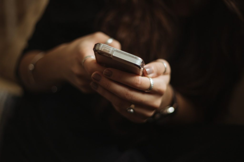 A closeup of someone holding a phone in their hands. They're wearing lots of rings and dark jumper.